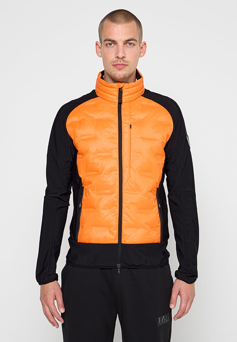 Padded jacket z pomarańczowym przodem i czarnymi rękawami, z wysokim kołnierzem, zamykanymi na zamek kieszeniami oraz eleganckim, sportowym krojem.