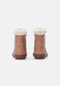 Botas sintéticas marrones con un collar de piel sintética, que presentan una textura suave, forma redondeada y acentos brillantes a lo largo de las costuras.