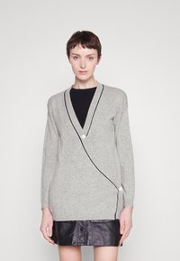 Cardigan gris avec un col en V, bord noir contrastant et fermeture à boutons blancs. Associé à une jupe en cuir noire.