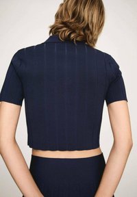 Námořnická modrá žebrovaná crop top s krátkými rukávy a límcem, který má vlnitý lem a texturovanou látku.