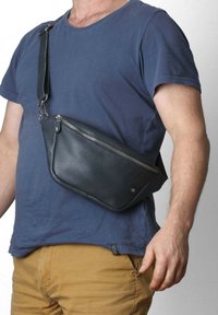 Borsa a tracolla nera in pelle con un design elegante, chiusura con zip e tracolla rimovibile; presenta un logo sottile e una texture liscia.