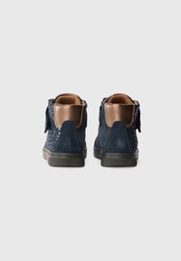 Navy suede ankle boots with a smooth brown leather accent, decorative perforations, and a textured black rubber outsole.