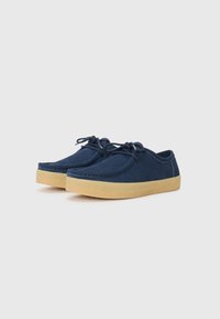 Navy blue suede shoes with round toes, laces, and textured beige rubber soles. Stitching visible along the edges, casual design.