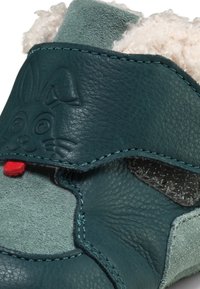 Scarpa in pelle teal con una soffice fodera bianca, design a forma di faccia di coniglio in un teal più scuro e un piccolo dettaglio di lingua rossa sul davanti.