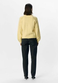 Yellow knitted sweater with textured sleeves, paired with dark jeans. Smooth finish, ribbed hem, and fitted shape. High-heeled shoes.