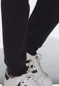 Svarta joggerbyxor i mjukt material med smal passform, tillsammans med vita sneakers med svarta ränder och texturerade såler.