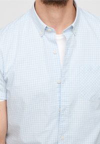 Světlomodrá kostkovaná košile s krátkými rukávy a límečkem na knoflíky, s přední kapsou a bílými knoflíky. Hladká bavlněná látka.