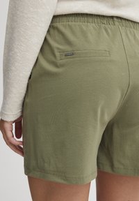 Olivgröna shorts med elastisk midja, med en bakficka och slät, strukturerad tyg. Accenterad med en liten märkesetikett.