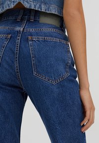 Džíny s vysokým pasem v modré denimové barvě s klasickým pětiokýnkovým designem, viditelným šitím a koženou značkou na zadním pasu.