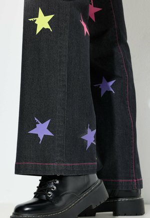 Wijd uitlopende zwarte jeans met kleurrijke sterren appliqués in roze, paars en geel, voorzien van roze stiksel en gecombineerd met zwarte platformlaarzen.
