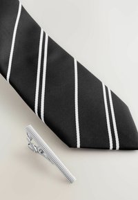 Black tie with white diagonal stripes, textured fabric. Silver tie clip with a patterned surface, positioned beside the tie.