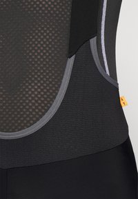 Débardeur de sport noir avec un panneau en maille texturée, des accents grisés contrastants et un design épuré. Étiquette avec le logo visible sur le côté.