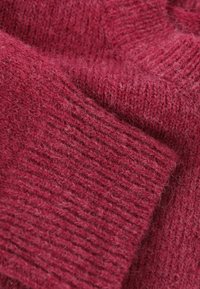 Pohodlný pletený sveter v hlbokej burgundskej farbe, ktorý má rebrovanú textúru a mäkký, chmýřový povrch. Materiál vyzerá teplo a lákavo.