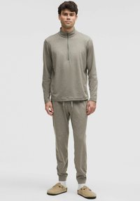 Lys grå, langærmet pullover med en kvart lynlås krave, parret med matchende sweatpants. Materialet ser blødt ud og har en afslappet pasform.