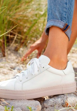 White leather sneakers with flat laces and a textured sole. The shoe has a low profile design and a soft, smooth finish.