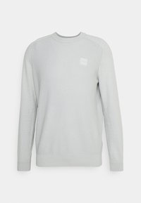 Jasnoszary sweter z długim rękawem, o prążkowanej teksturze i okrągłym dekolcie. Posiada małą, kwadratową łatę z logo na piersi.