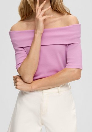 Różowa bluzka z opuszczonymi ramionami o prążkowanej fakturze, krótkich rękawach i luźnym kroju, zestawiona z białymi, wysokim stanem spodniami.