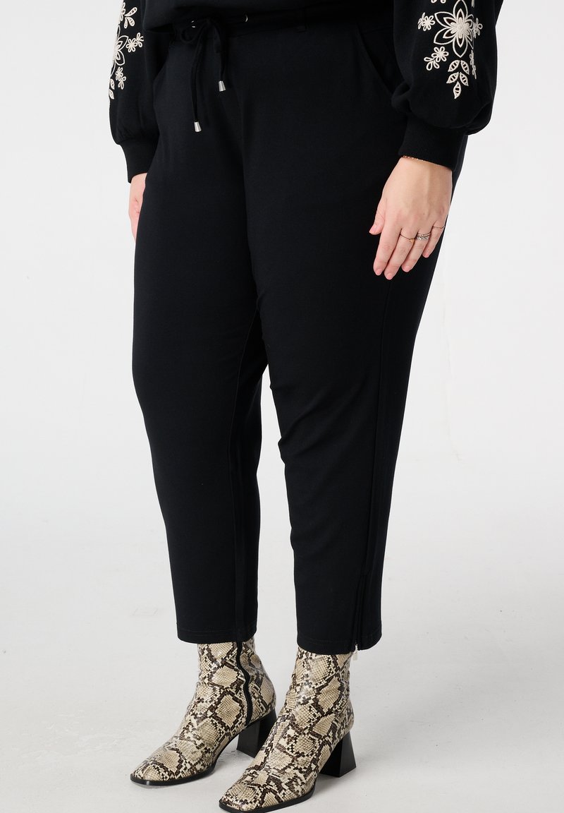 Zwarte taps toelopende broek met een trekkoord in de taille. Gecombineerd met beige enkellaarsjes met slangenprint en blokhak. Gestructureerde, gladde stof.