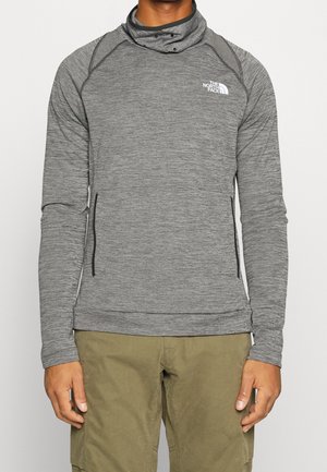 Grijze lange mouw trui met een hoge kraag, voorzien van een gestructureerde stof en zwarte zijzakken met rits. Logo op de linkerborst.