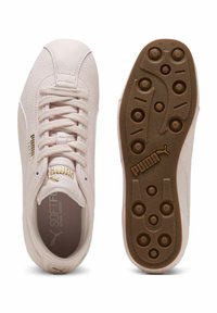 Sneakersy Puma o teksturowanej, jasnoróżowej cholewce, sześciu oczkach na sznurówki oraz brązowej gumowej podeszwie z okrągłymi punktami przyczepności.