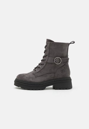 Γκρι suede ankle boots με στρογγυλή μύτη, κορδόνια μπροστά, διακοσμητική στρογγυλή αγκράφα και χοντρή μαύρη καουτσούκ σόλα. Διαθέτει λαβή στο πίσω μέρος.