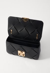 Schwarze Ledertasche mit einem gesteppten Design, goldfarbener Hardware und einem Druckverschluss. Das Innere verfügt über ein Markenlogo und ein leeres Fach.