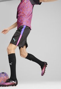 Czarne spodenki sportowe z purpurowymi i różowymi akcentami, w zestawie z koszulą w purpurowo-czerwoną wzory oraz czarnymi korkami, obok wielokolorowej piłki.
