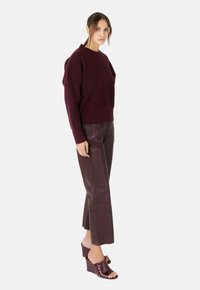 Bordeaux trui van breiwerk met een ronde hals en een losse pasvorm, gecombineerd met donkerbordeaux leren cropped broek en open teen sleehakken.