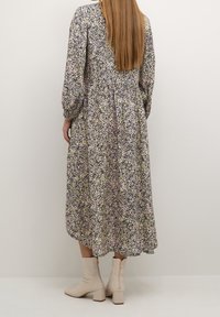 Abito midi floreale in viola, verde e bianco con maniche a sbuffo e vita arricciata. Indossato con stivali alla caviglia a tacco blocco color beige chiaro.