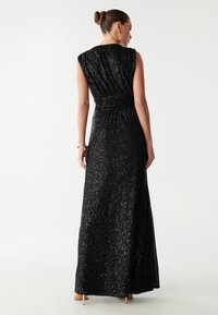 Sort palietteret maxikjole med rynket bodice og kortærmer. Glat tekstur, flydende silhuet og let udstyret nederdel.