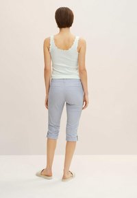 Pantalones recortados azul claro con puños doblados y bolsillos traseros, combinados con una camiseta sin mangas blanca de canalé con bordes en forma de ondas.