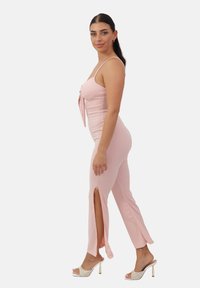 Mono rosa con diseño ajustado, detalle con lazo en el frente, aberturas laterales y tejido suave. Combinado con tacones de punta abierta que cuentan con una correa con estampado.