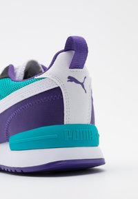 Baskets violettes et blanches avec un accent turquoise texturé, arborant un logo Puma et une languette au talon. Le design est sportif et moderne.
