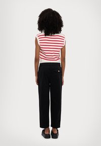 Top de tirantes a rayas con un patrón de punto rojo y blanco, combinado con pantalones de pierna ancha negros. Modelo lleva zapatos de plataforma negros, visto desde atrás.