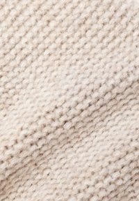 Pehmeä villakankaan beige sävyissä, jossa on teksturoitu neulekuvio vaihtelevilla silmukkakokoilla ja hieman pörröinen pinta.