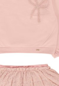 Felpa rosa con dettagli in raso a forma di fiocco e gonna elastica coordinata con sovrapposizione trasparente e motivi dorati.