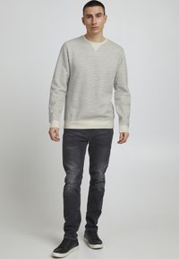 Lys grå hettegenser med teksturert materiale, ribbede ermer og kant. Sammen med mørkegrå slim-fit jeans og svarte treningssko.