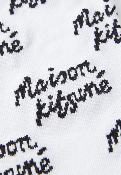 Valge kangas, millel on korduv must tekst "maison kitsuné" käsitsi kirjutatud stiilis fondis. Tekstuur näeb välja sile ja kudum.