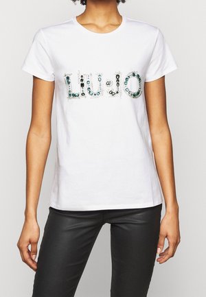 Valkoinen puuvillainen t-paita, jossa "LIU-JO"-teksti koristeltu värikkäillä jalokivillä. Lyhyet hihat ja pyöreä pääntie, normaalimittainen istuvuus.