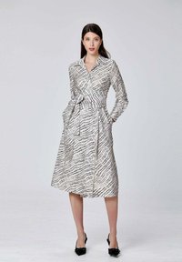 Robe blanche avec un motif linéaire noir, manches longues, col à boutons, ceinture à la taille et poches latérales, longueur genou, texture de tissu lisse.