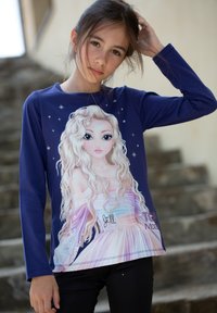 Maglietta a maniche lunghe blu navy con un design stampato di un personaggio dai capelli biondi, che indossa un vestito pastello e ha dettagli a forma di stella.