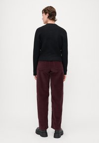 Svart kortärmad tröja, vinröda kordbyxor och kraftiga svarta platåskor. Byxorna har bakfickor och en texturerad yta.