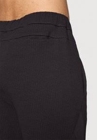 Close-up of a person wearing textured black athletic pants with an elastic waistband and side pocket.