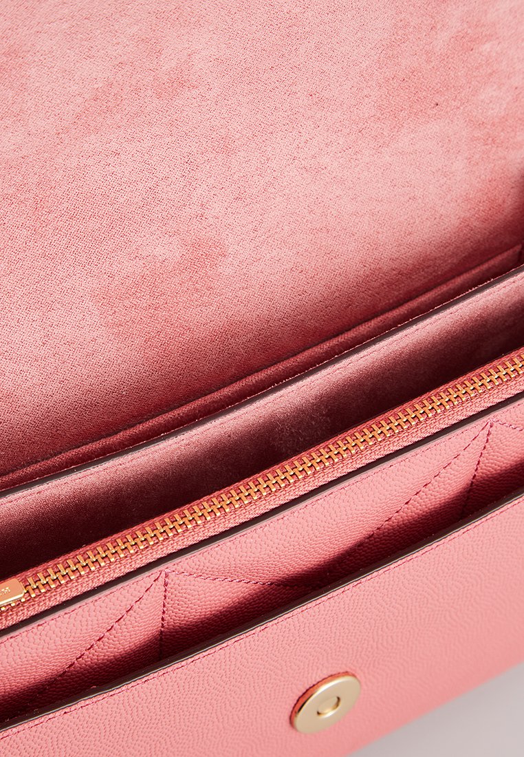 Interior de un bolso de mano de cuero texturizado rosa con un forro suave y mullido. Presenta un cierre de cremallera dorada y un bolsillo interior visible.