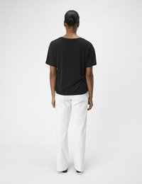 Sort kortærmet t-shirt med en afslappet pasform, kombineret med hvide højtaljede straight-leg bukser. Enkel design uden synlige mønstre.