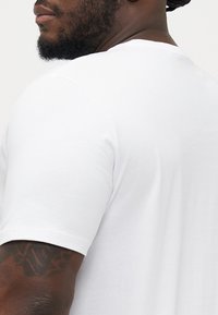Witte T-shirt met korte mouwen en een ronde halslijn, gemaakt van een gladde, lichte stof. Heeft een getailleerd ontwerp en subtiele stikdetails.