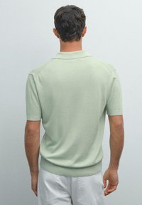 Polo a maniche corte in morbido materiale a maglia verde chiaro, con colletto e orlo a coste, dalla texture liscia.