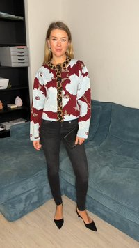 Πλεκτό πουλόβερ με κόκκινο και μπλε λουλουδένιο σχέδιο, λεπτομέρειες σε λεοπάρ μοτίβο, μαύρα στενά τζιν και μαύρες μυτερές γόβες, που στέκεται σε υφασμάτινο καναπέ.