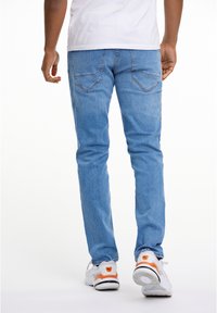 Light blue, tapered denim jeans with back pockets; paired with white sneakers featuring orange accents. Smooth texture and casual design.