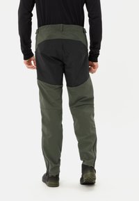 Buitenbroek met een zwart bovenstuk en een olijfgroen onderstuk. Voorzien van ritsen bij de enkels en een aansluitende pasvorm. Gemaakt van duurzame materialen.